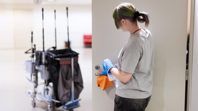 Henkilö puhdistaa oven kahvaa, taustalla siivouskärry