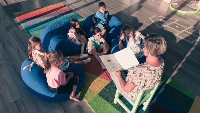 Lapset kuuntelevat kirjaa lukevaa opettajaa keskittyneesti.