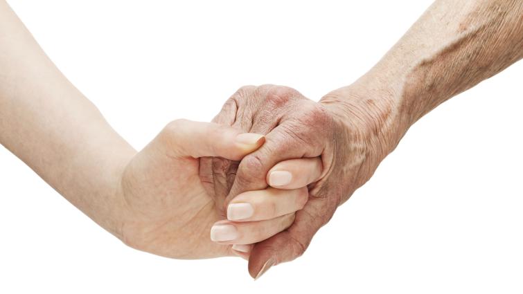 Ikääntyneen ihmisen käsi pitämässä nuoremman ihmisen kädestä kiinni
