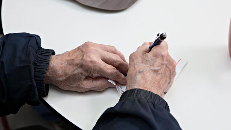 Vanhuksen kädet kirjoittamassa paperilapulle