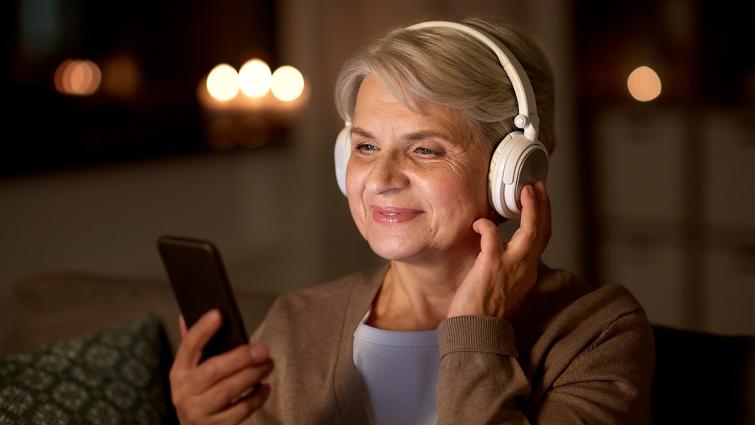 Nainen kuuntelee kuulokkeet korvilla ja katsoo puhelinta.